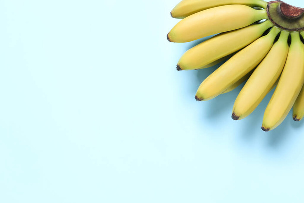 Bunch of ripe baby bananas on light blue background, top view. Space for text - Фото, изображение
