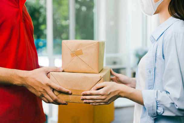 close-up levering man in rood uniform leveren dienst pakket doos naar klant vrouw thuis - Foto, afbeelding