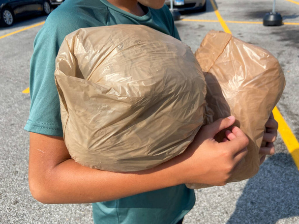 Jovem carrega feixes empacotados de sacos de plástico de varejo através de estacionamento para mercearia para reciclagem na loja drop off  - Foto, Imagem