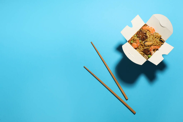 Box of wok noodles with seafood and chopsticks on turquoise background, flat lay. Space for text - Photo, image