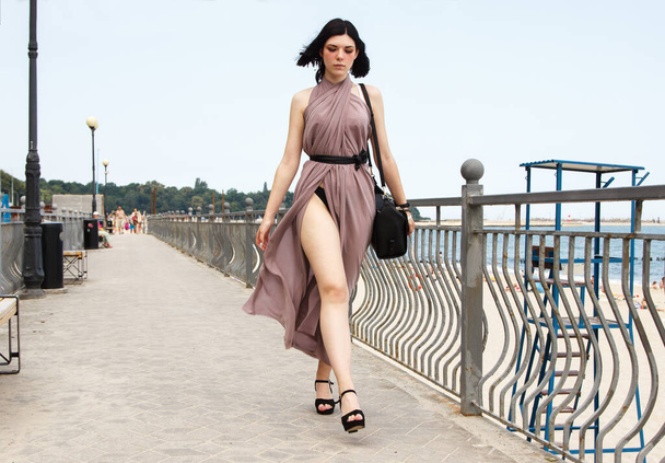 mladá krásná brunetka žena v béžových šatech chůze na chodníku v létě - Fotografie, Obrázek
