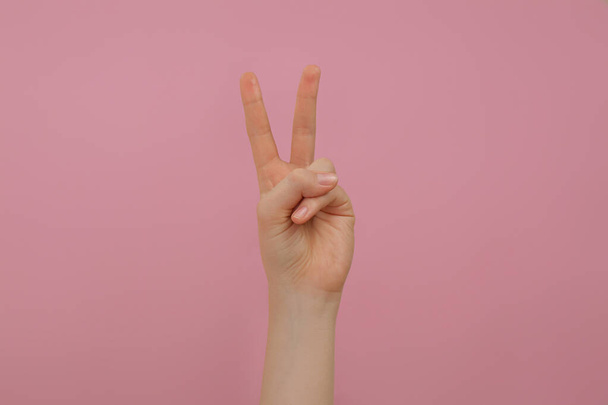 Woman showing two fingers on pink background, closeup - Фото, изображение