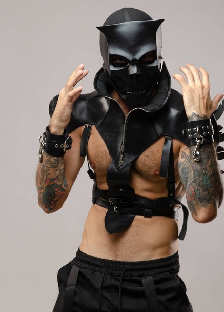 a man in a bdsm demon skull mask, dressed in a leather cloak with leather bracelets and straps on his body - Photo, image