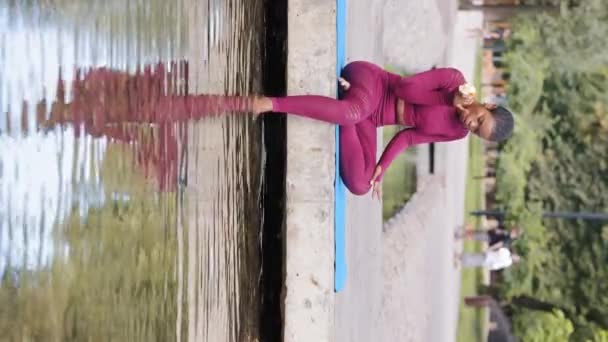 Mladá mírumilovná Afroameričanka ve sportovním oblečení odpočívající po cvičení v letním parku. Krásné tisícileté černošky dívka relaxační sedí venku ponořené nohy do studené vody, jí jablka. Svislé video - Záběry, video