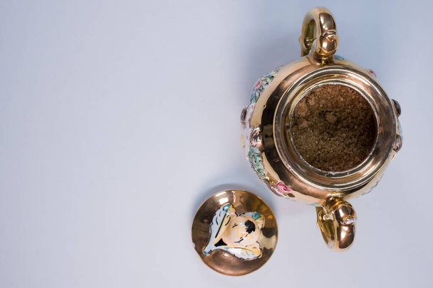 A top view of brown sugar in a vintage pot with a lid, placed on a white surface - Foto, afbeelding