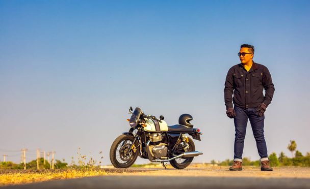 オートバイの夏の旅行、黒い革のジャケットのオートバイの運転手は、ヴィンテージのオートバイが延びた道路上に立って、選択的な焦点 - 写真・画像