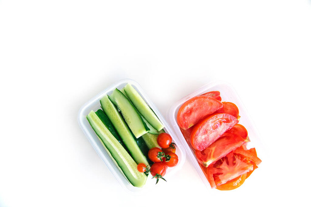 Sliced vegetables in plastic containers on a white background. Cucumbers and tomatoes are in containers. Healthy and proper nutrition. Packed lunch for work or travel. - Zdjęcie, obraz
