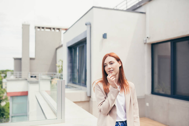young caucasian woman standing on the terrace of a modern office or balcony at home and smokes marijuana. Business lady smoking cannabis. female relieves stress at work a light drug. businesswoman - Foto, Bild