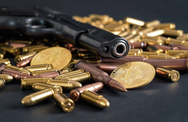 Bronze and brass gun bullets scattered on dark table, black pistol barrel, golden bitcoin coins near - illegal use of cryptocurrency to purchase weapon concept - Photo, image