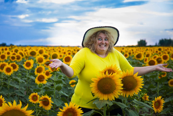 fat woman in a sunflower field laughs, enjoys life and makes a gesture of surprise - Foto, Imagen