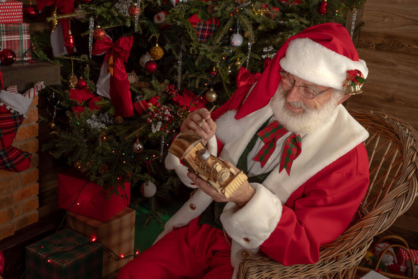 Santa Claus haciendo juguetes en el taller en el interior festivo de la casa de madera, humor alegre de Año Nuevo Espíritu de la Navidad. Hombre mayor con barba blanca real cosplay Papá Noel. - Foto, Imagen
