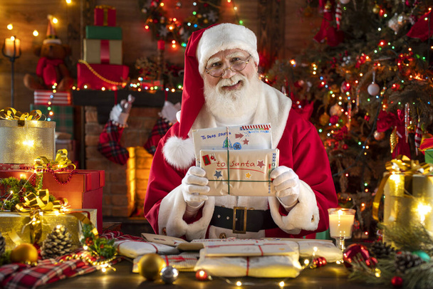 Santa Claus rejoicing with letters and mail in his post office indoors Log Cabin at the North Pole. Grandpa getting ready for Christmas Eve Party. Senior model with real beard cosplay Father Christmas - Photo, Image