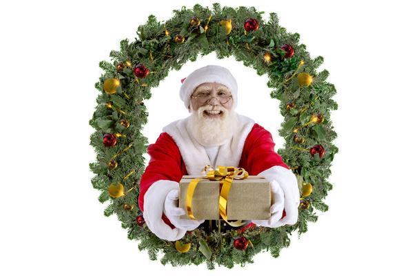 Santa Claus with gift boxes in Christmas wreath with golden sparks, garlands, New Year's decor. Grandpa getting ready for Christmas Eve Party. Senior model with real beard cosplay Father Christmas. - Photo, Image