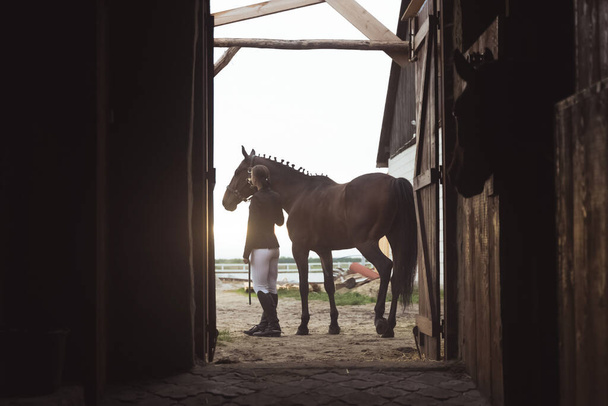 Hevonen nainen seisoo hänen tumma Bay Horse ulkopuolella Stable päivällä - Valokuva, kuva