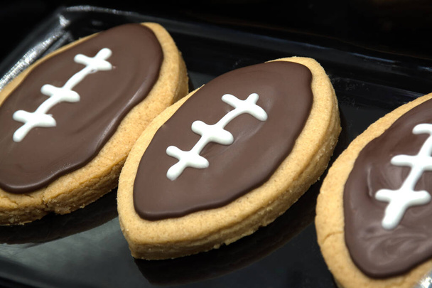 Hand taking cookie from plate. Football shape cookies on plate. Home made cookies concept. American sport concept. Super Bowl party cookies. - Photo, image