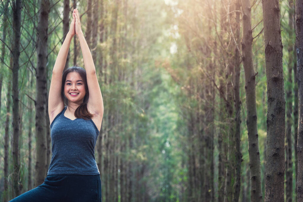 Beautiful happy young female woman relaxation standing outdoor fitness exercise yoga in forest tree nature park with copy space - 写真・画像
