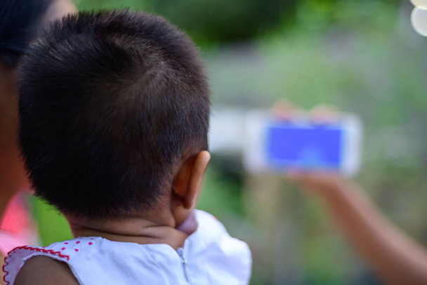 Маленький ребенок смотрит мультфильм на мобильном телефоне, родители используют мобильные видео, чтобы остановить плач младенцев. Концепция развития детского обучения. Девушка держит мобильное устройство перед ребенком. - Фото, изображение