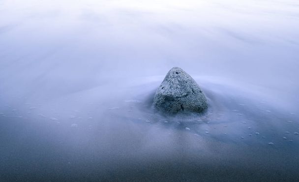 Immobile Korallenfelsbrocken am Sandstrand Langzeitbelichtungsfoto. spiralförmige Dunkelheit, die ins Zentrum des Interesses führt, seidig glatte weiße Meeresformen und Wellen um den Felsen herum. - Foto, Bild