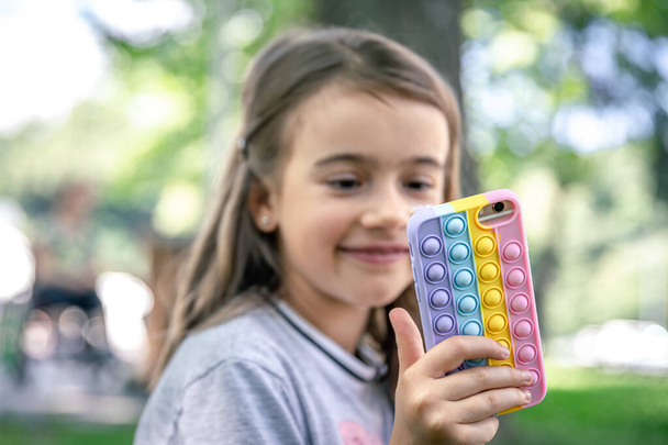 Una bambina tiene in mano un telefono in una custodia con brufoli pop it, un giocattolo anti stress alla moda. - Foto, immagini