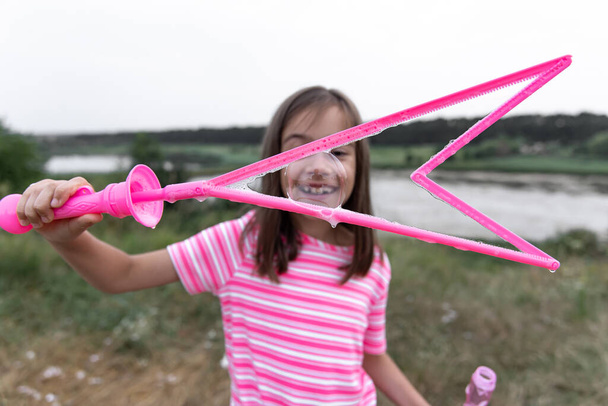 Una piccola ragazza divertente soffia bolle di sapone in estate in un campo, attività estive all'aperto. - Foto, immagini