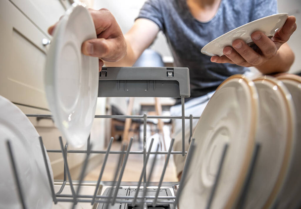 A man in front of an open dishwasher takes out clean dishes after washing. - Photo, Image