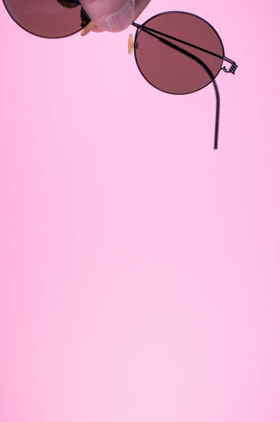 A vertical shot of a hand holding sunglasses on a pink background - Φωτογραφία, εικόνα