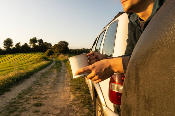 A closeup shot of a Hispanic male with a cup sitting in a field next to a car - Photo, image
