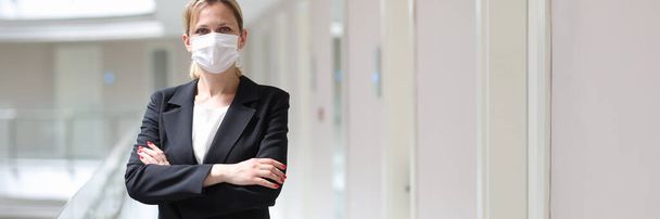 Liikenainen lääketieteellinen suojaava naamio seisoo taitettu kädet hotellin käytävällä - Valokuva, kuva