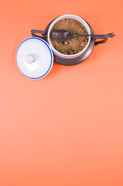 A vertical shot of brown sugar in a pot with a lid, placed on an orange surface - Фото, зображення
