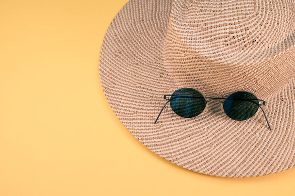 A top view of a straw hat and sunglasses on a yellow surface - Photo, image