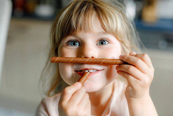 Portré egy vidám kisiskolás lányról, aki csokis gofris tekercset tart. Mosolygó éhes kisgyerek édes keksz ostyával. Édes cukor kakaógofri. - Fotó, kép