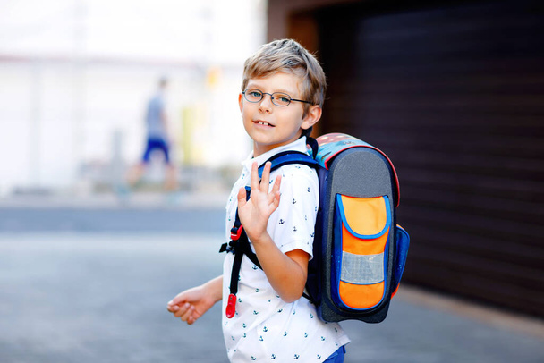 Onnellinen pikkupoika, jolla on lasit ja reppu tai olkalaukku. Koulupoika on matkalla kouluun. Terveen suloisen lapsen muotokuva ulkona. Oppilas, oppilas, takaisin kouluun. Peruskoulun ikä - Valokuva, kuva