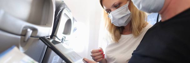 Koruyucu maskeli bir adam ve kadın uçakta uçuyor ve dijital tablet ekranına ve grafikli belgelere bakıyor. - Fotoğraf, Görsel