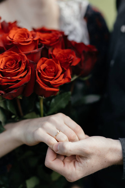 Recién casados novia y novio toman de la mano en el fondo de un ramo de flores de rosas rojas, primer plano de ternura y romance. - Foto, imagen