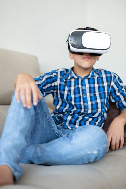 10代の若者が自宅で仮想現実の眼鏡をかけてソファに座っている。彼は集中して楽しまれている. - 写真・画像