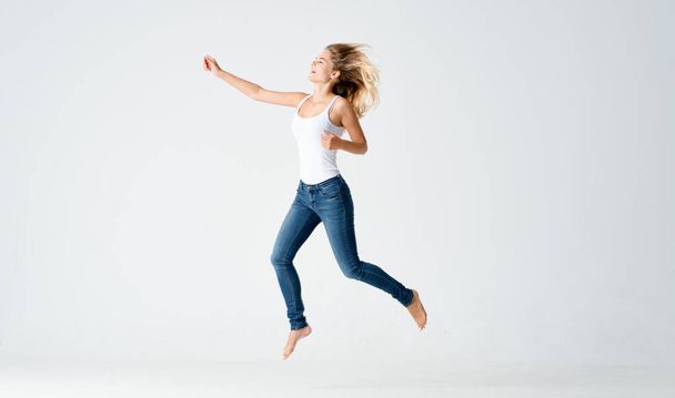 pretty woman in jeans movements dance barefoot light background - Fotoğraf, Görsel