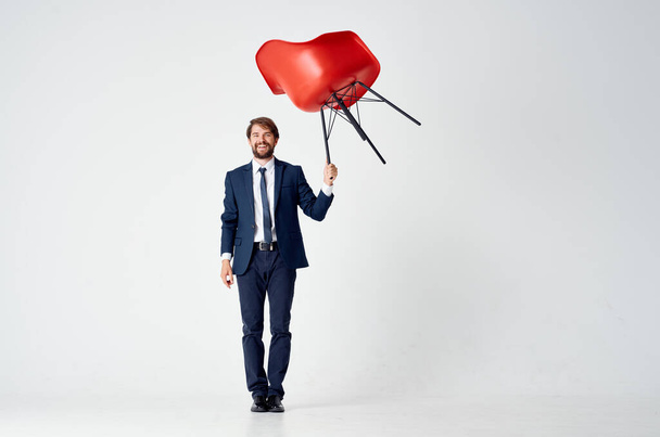 business man in a suit with a red chair in his hands above his head emotions - Photo, Image