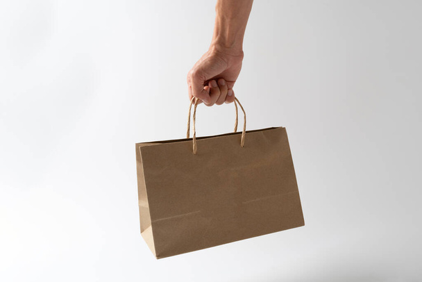 Man holding paper shopping bag on whie background - Foto, afbeelding