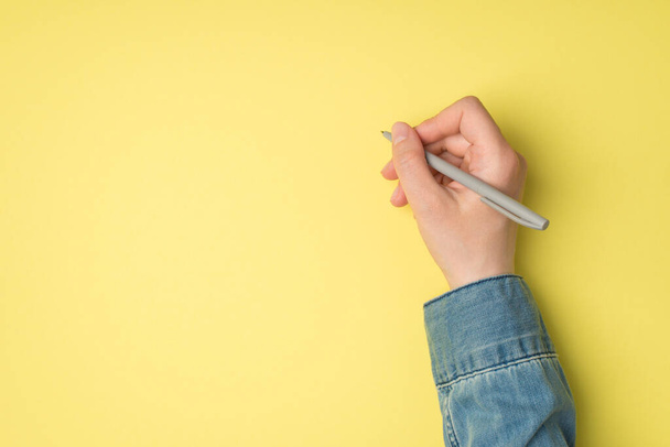 First person top view photo of female hand holding grey pen on isolated yellow background with copyspace - Valokuva, kuva