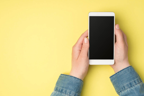 First person top view photo of female hands holding cellphone on isolated yellow background with blank space - Photo, Image