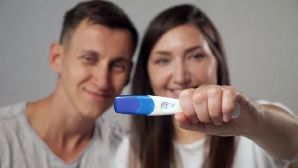 lähikuva positiivisesta raskaustestistä onnellisen miehen ja naisen hämärtyneellä taustalla, hidastettuna - Materiaali, video
