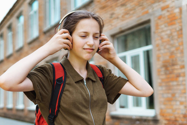 Joyeux écolière en route pour l'école. Elle écoute de la musique avec des écouteurs. Éducation et concept de retour à l'école - Photo, image