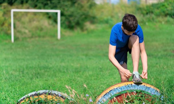 10代の男の子が屋外で運動したり、庭で運動したり、靴ひもを結んだり、暖かくて健康的なライフスタイルをしています - 写真・画像