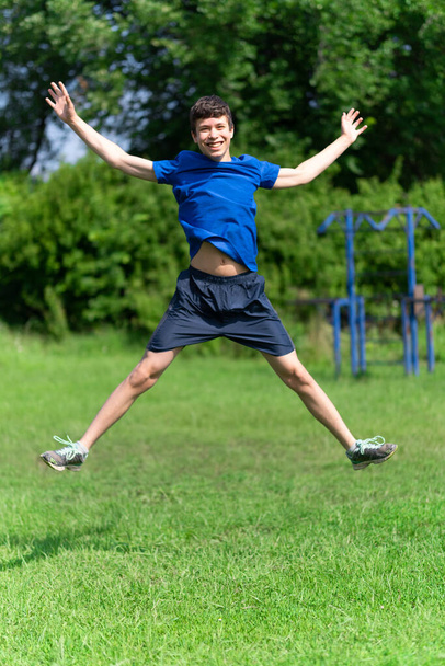 teenage boy exercising outdoors, sports ground in the yard, he jumps high, healthy lifestyle - Fotó, kép