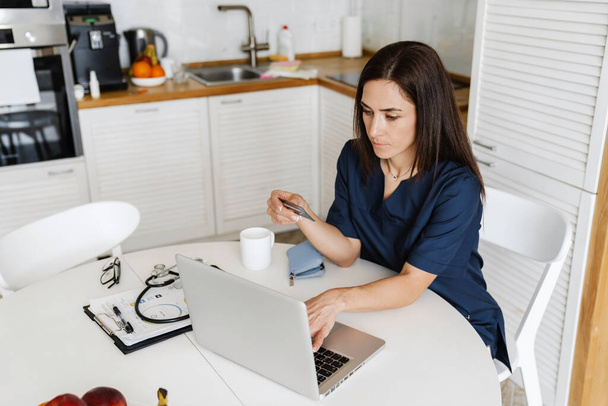 Focalisé femme médecin à l'aide de carte de crédit et ordinateur portable tout en étant assis à la maison - Photo, image