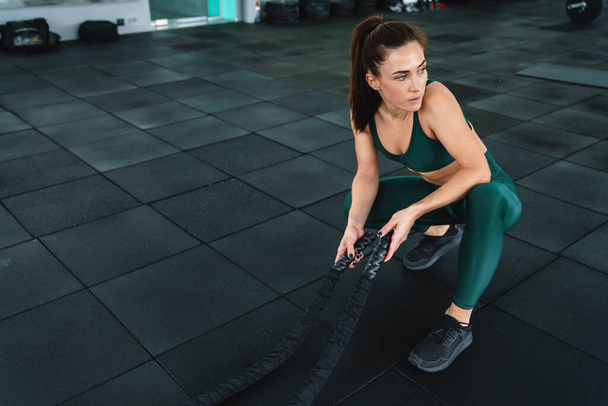 White sportswoman doing workout with battle ropes in gym - Foto, Imagem