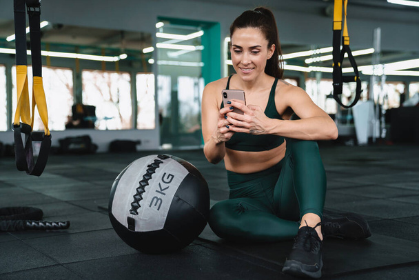 White sportswoman using cellphone while working out with medicine ball in gym - Foto, Imagem