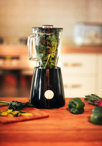 Close up photo of green vegetable smoothie blender machine in kitchen with kale leaves inside ready for grinding process. Concept of healthy diet, detoxification, healthy lifestyle, vegetarianism - Photo, Image