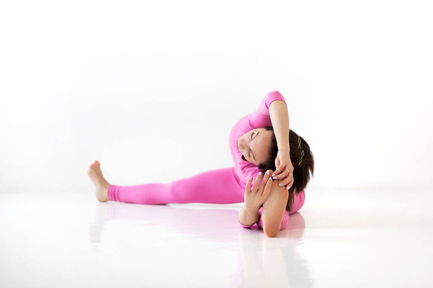 Young slender fit woman in pink long bodysuit performing yoga pose, isolated over white studio background. Healthy lifestyle, sport and fitness concept - Photo, Image