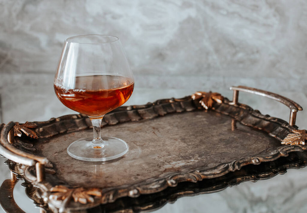 Egy pohár brandy vagy konyak fémtálcán. Szürke kő háttér másolási hellyel. Vízszintes fénykép. - Fotó, kép